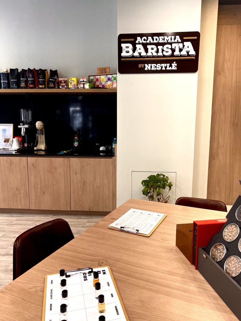 Academia Barista by Nestlé: espacio de formación en café con mesa de cata, aromas y evaluación sensorial. Estantería con variedades de café y té, junto a equipos de barismo